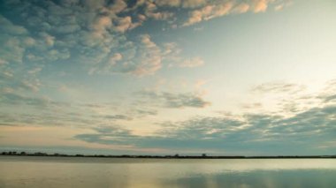 Bright sunset rays of the sun shine through thick evening white clouds over the blue calm Black Sea. UHD 8k video timelaps