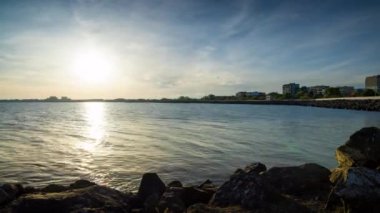 The embankment with rocky small dark stones passes over the bay of a calm deep Black sea against the backdrop of a sunset evening sunny sky. UHD 8k video timelaps