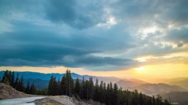 A mountain valley with mountain peaks of the Rhodope Mountains covered with dense spruce dark forests is shaded under a cloudy evening sunset bright sunny sky. UHD 8K video timelaps