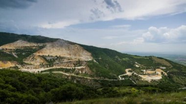 Industrial quarry for extraction of minerals with equipment and machines, and intermountain winding road passing by, in Rhodope Mountains covered with coniferous forests. UHD 8K video timelaps