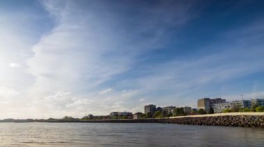 The embankment with rocky small dark stones passes over the bay of a calm deep Black sea against the backdrop of a sunset evening sunny sky. UHD 8k video timelaps