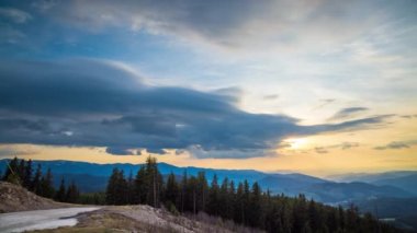 A mountain valley with mountain peaks of the Rhodope Mountains covered with dense spruce dark forests is shaded under a cloudy evening sunset bright sunny sky. UHD 8K video timelaps