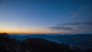 Cloudy weather over low hills covered with spruce evergreen forests in Rhodope Mountains against backdrop of sunset sky, and mystical thick white fog between mountain ranges. UHD 8K video timelaps