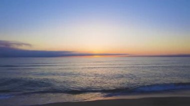 Calm blue boundless Black Sea with cool water reflecting light and sandy wild empty beach nearby, against cloudy colored sky with white clouds and bright dawn sun. UHD 4K video timelaps