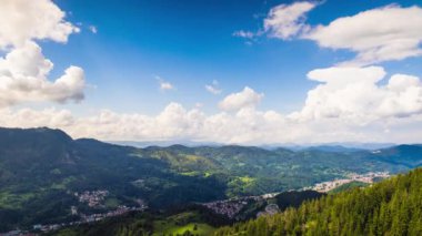 Unusual white fluffy clouds float across the blue evening sky with sunlight over the mountain valley of the Rhodope Mountains with the small village of Smolyan in the intermountain. UHD 8K video