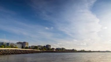 The embankment with rocky small dark stones passes over the bay of a calm deep Black sea against the backdrop of a sunset evening sunny sky. UHD 8k video timelaps