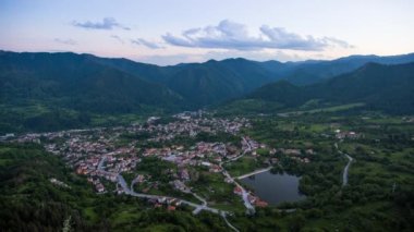 Unusual white fluffy clouds float across the blue evening sky with sunlight over the mountain valley of the Rhodope Mountains with the small village of Smolyan in the intermountain. UHD 8K video