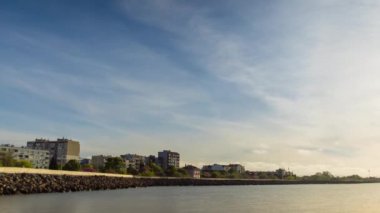 The embankment with rocky small dark stones passes over the bay of a calm deep Black sea against the backdrop of a sunset evening sunny sky. UHD 4k video timelaps