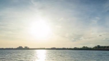 The embankment with rocky small dark stones passes over the bay of a calm deep Black sea against the backdrop of a sunset evening sunny sky. UHD 4k video timelaps