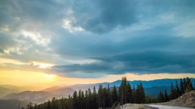 A mountain valley with mountain peaks of the Rhodope Mountains covered with dense spruce dark forests is shaded under a cloudy evening sunset bright sunny sky. UHD 4K video timelaps