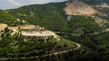 Industrial quarry for extraction of minerals with equipment and machines, and intermountain winding road passing by, in Rhodope Mountains covered with coniferous forests. UHD 4K video timelaps