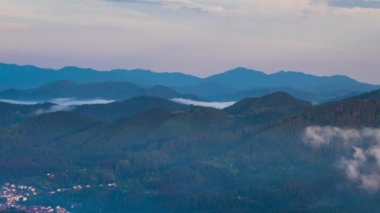 Green spring mountain valley sheltered by vegetation and spruce dark forests with small old village Smolyan, with grassy meadows where hungry motley sheep graze. UHD 4K video timelaps