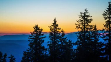 A mountain valley with mountain peaks of the Rhodope Mountains covered with dense spruce dark forests is shaded under a cloudy evening sunset bright sunny sky. UHD 4K video timelaps