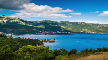 Top view of resort seaside town of Budva with various holiday hotels and fashionable beaches and boats with ships sail from coast to coast along bay in the light of setting sun. UHD 4K video timelaps