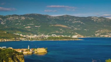 Top view of resort seaside town of Budva with various holiday hotels and fashionable beaches and boats with ships sail from coast to coast along bay in the light of setting sun. UHD 4K video timelaps