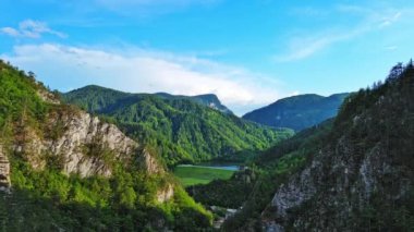 Dar, dolambaçlı bir dağ yolu, Rodop Dağları 'ndaki mavi bulutlu bir gökyüzünün altında yeşil yay dağ bitkilerinin bulunduğu dağ kanyonlarından geçer. UHD 4K video gerçek zamanlı