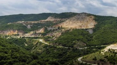 Industrial quarry for extraction of minerals with equipment and machines, and intermountain winding road passing by, in Rhodope Mountains covered with coniferous forests. UHD 4K video timelaps