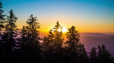 A mountain valley with mountain peaks of the Rhodope Mountains covered with dense spruce dark forests is shaded under a cloudy evening sunset bright sunny sky. UHD 4K video timelaps