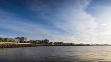 The embankment with rocky small dark stones passes over the bay of a calm deep Black sea against the backdrop of a sunset evening sunny sky. UHD 4k video timelaps