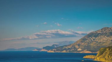 The steep slopes of the Montenegrin Mountains with resort hotels, tourist historical sites and summer green vegetation are washed by calm blue dark waters of the Adriatic Sea. UHD 4K video timelaps
