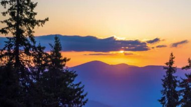 A mountain valley with mountain peaks of the Rhodope Mountains covered with dense spruce dark forests is shaded under a cloudy evening sunset bright sunny sky. UHD 4K video timelaps