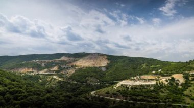 Industrial quarry for extraction of minerals with equipment and machines, and intermountain winding road passing by, in Rhodope Mountains covered with coniferous forests. UHD 8K video timelaps