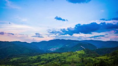 Çok renkli akşam gökyüzü, küçük bulutlar ve güneşli gün batımı ile Rodop Dağları 'nın dağ vadisinde küçük, dağlararası bir köyle birlikte. UHD 8K video zaman çizelgeleri