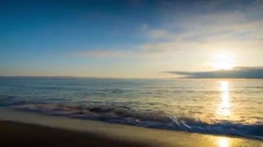 Calm blue boundless Black Sea with cool water reflecting light and sandy wild empty beach nearby, against cloudy colored sky with white clouds and bright dawn sun. UHD 4K video timelaps