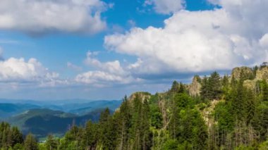 High rocky wild mountain range of Rhodope Mountains covered with vegetation, against backdrop of mountain valley covered with dark spruce forests and blue cloudy sky. UHD 4K video timelaps