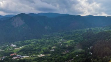 View from high rock to old village Smolyan with green meadows for cattle walking and houses, between mountain range of Rhodope Mountains sheltered by spruce forests. UHD 4K video footage timelaps