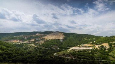 Industrial quarry for extraction of minerals with equipment and machines, and intermountain winding road passing by, in Rhodope Mountains covered with coniferous forests. UHD 4K video timelaps