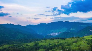Multicolored evening sky with small clouds and sunny sunset light over the mountain valley of the Rhodope Mountains with a small lonely intermountain village. UHD 4K video timelaps