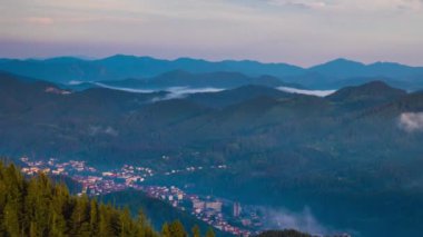 Green spring mountain valley sheltered by vegetation and spruce dark forests with small old village Smolyan, with grassy meadows where hungry motley sheep graze. UHD 4K video timelaps