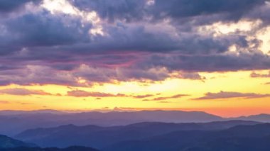 Cloudy weather over low hills covered with spruce evergreen forests in Rhodope Mountains against backdrop of sunset sky, and mystical thick white fog between mountain ranges. UHD 4K video timelaps
