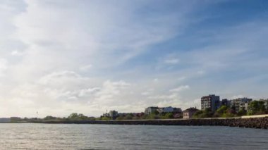 The embankment with rocky small dark stones passes over the bay of a calm deep Black sea against the backdrop of a sunset evening sunny sky. UHD 4k video timelaps