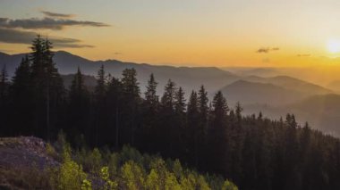 A mountain valley with mountain peaks of the Rhodope Mountains covered with dense spruce dark forests is shaded under a cloudy evening sunset bright sunny sky. UHD 4K video timelaps