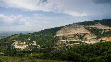 Industrial quarry for extraction of minerals with equipment and machines, and intermountain winding road passing by, in Rhodope Mountains covered with coniferous forests. UHD 4K video timelaps