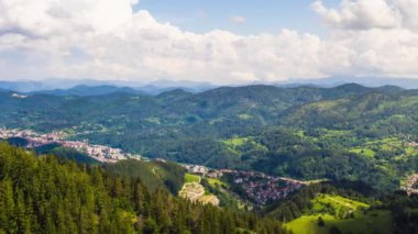 View from high rock to old village Smolyan with green meadows for cattle walking and houses, between mountain range of Rhodope Mountains sheltered by spruce forests. UHD 4K video footage timelaps