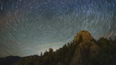 Rocky steep peak of a high mountain with dense dark spruce forests on the slopes against the backdrop of a magical starry clear night sky. UHD 4K video timelaps