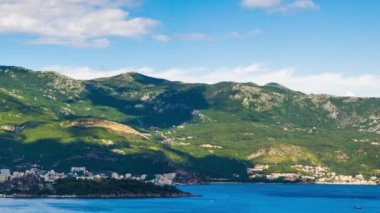 Top view of resort seaside town of Budva with various holiday hotels and fashionable beaches and boats with ships sail from coast to coast along bay in the light of setting sun. UHD 4K video timelaps