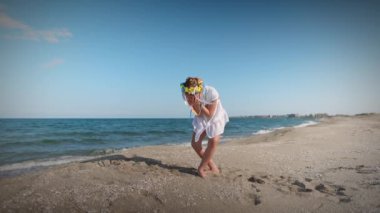 Ukraynalı beyaz gömlekli, çiçekli Ukrayna çelengi giyen, çok renkli, parlak kurdeleli, günbatımında Karadeniz kıyısında dans eden küçük bir kız. UHD Video yavaş çekim 4K