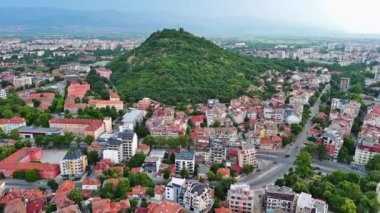 Ancient intermountain town Plovdiv with old residential houses and green fields, against backdrop of Rhodope Mountains and hills covered with spruce forests and overcast sky. UHD 4K video realtime