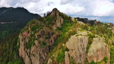 High rocky wild mountain range of Rhodope Mountains covered with green vegetation, against backdrop of mountain valley covered with dense dark spruce forests and blue cloudy sky. UHD 4K video realtime