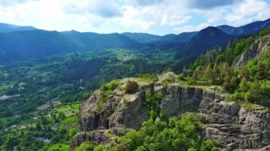 High rocky wild mountain range of Rhodope Mountains covered with green vegetation, against backdrop of mountain valley covered with dense dark spruce forests and blue cloudy sky. UHD 4K video realtime