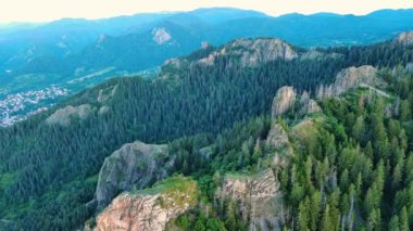 High rocky wild mountain range of Rhodope Mountains covered with green vegetation, against backdrop of mountain valley covered with dense dark spruce forests and blue cloudy sky. UHD 4K video realtime