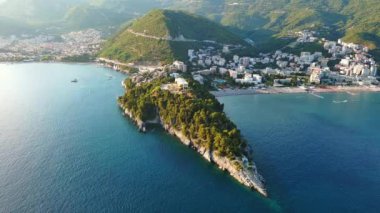 Budva ve Becici tatil beldeleri, sakin Adriyatik Denizi yakınlarında lüks oteller ve rahat plajlarla Karadağ Dağları ve mavi gökyüzüne karşı. UHD Video gerçek zamanlı 4K