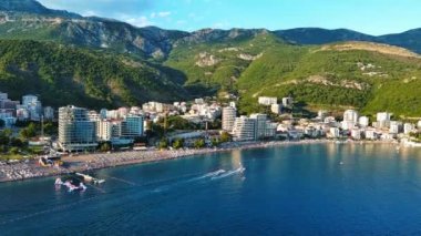 Budva ve Becici tatil beldeleri, sakin Adriyatik Denizi yakınlarında lüks oteller ve rahat plajlarla Karadağ Dağları ve mavi gökyüzüne karşı. UHD Video gerçek zamanlı 4K
