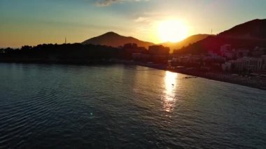 Budva ve Becici tatil beldeleri, sakin Adriyatik Denizi yakınlarında lüks oteller ve rahat plajlarla Karadağ Dağları ve mavi gökyüzüne karşı. UHD Video gerçek zamanlı 4K