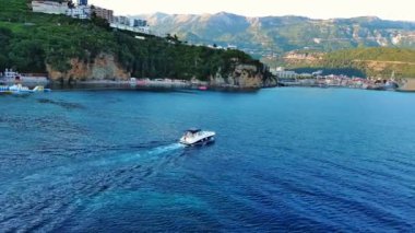 Gezintiler için küçük beyaz bir motorlu tekne yüksek tehlikeli uçurum yamaçlarının altında turkuaz deniz suyunda yüzüyor. UHD Video gerçek zamanlı 4K