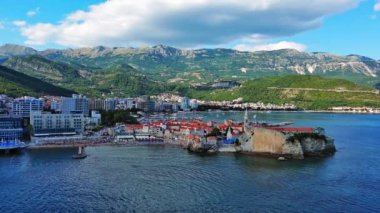 Küçük gemileri ve tekneleri olan deniz turizm limanı antik tarihi Budva adası yakınlarındaki Adriyatik Denizi 'nde romantik bulutlu gökyüzüne karşı. UHD Video gerçek zamanlı 4K